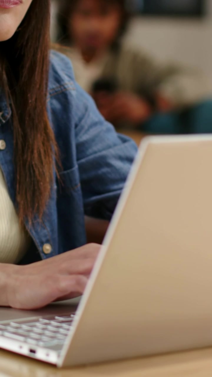 Video verticale: Primo piano di una donna in camicia di jeans che digita sul portatile in un caffè con telefono e pianta.