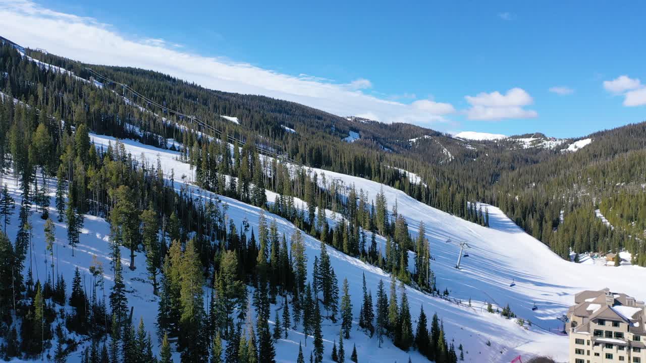 Big Sky, Montana comes alive with winter ski action in this drone view, showing chair lifts filled with skiers, snowy slopes below, and mountain scenery stretching into the distance