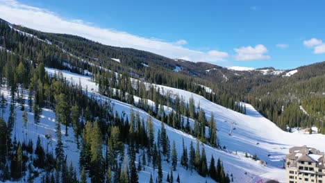 big sky, montana comes alive with winter ski action in this drone view, showing chair lifts filled with skiers, snowy slopes below, and mountain scenery stretching into the distance