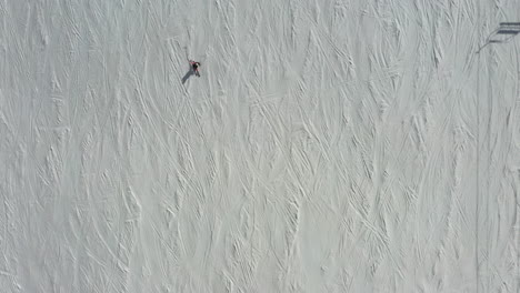 person skiing down hill slope fast, aerial top down follow view