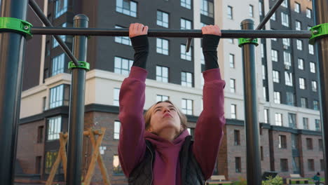 close up of gym trainer working out on horizontal pull up bar in park setting with autumn foliage and urban backdrop showcasing forearm strength focus and control during calisthenics session