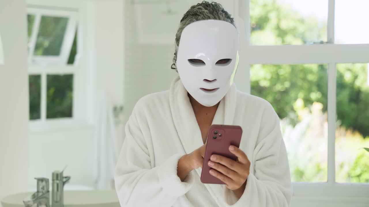 Eine afroamerikanische Frau begutachtet sich, legt im Bademantel am Waschbecken eine Maske an und tippt auf ihr Telefon, um eine Therapie zu starten.