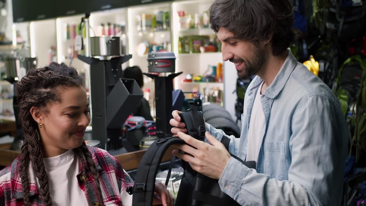 una pareja joven está eligiendo una nueva mochila, una mujer intentando una en los hombros