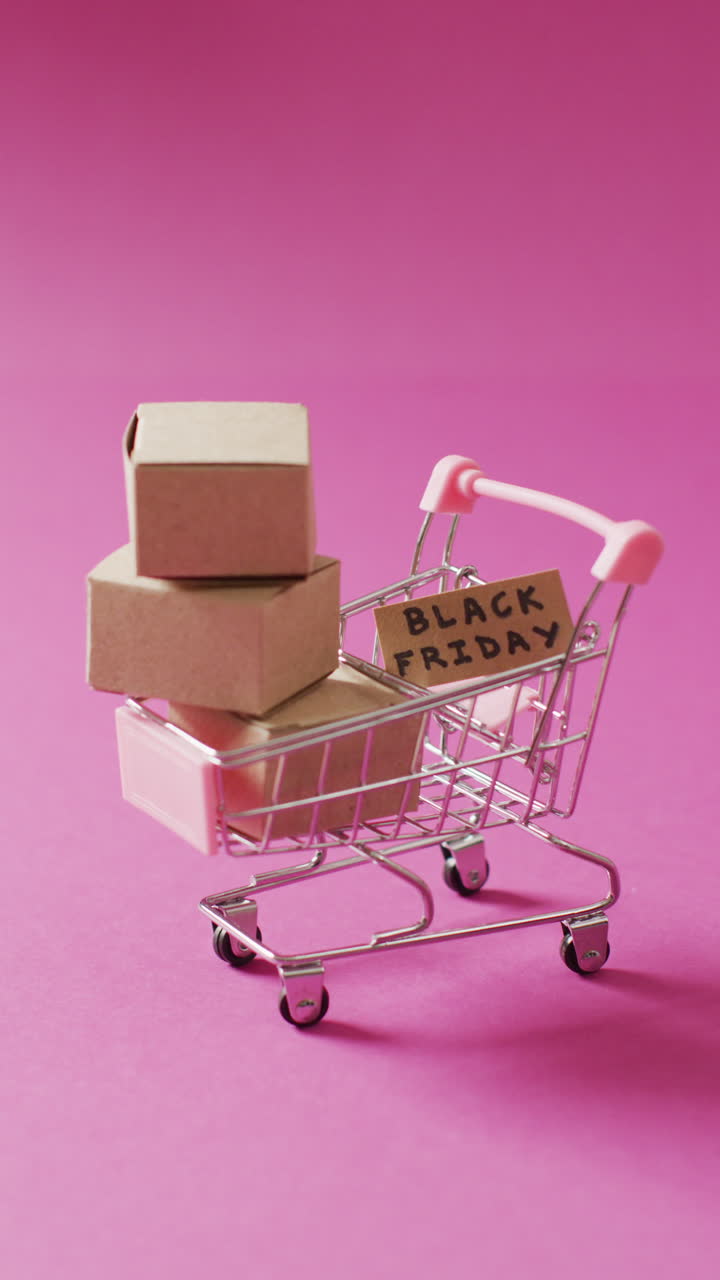 video vertical de texto de viernes negro en cartón y cajas en el carrito de compras en fondo rosa
