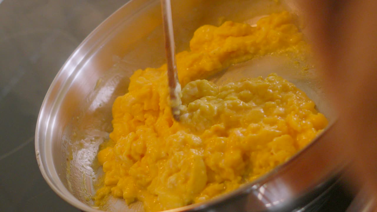 Top View of Chef Stirring Creamy Scrambled Eggs with Spatula Kitchen Utensil in Natural Light with Shallow DOF. Cooking Food Footage.