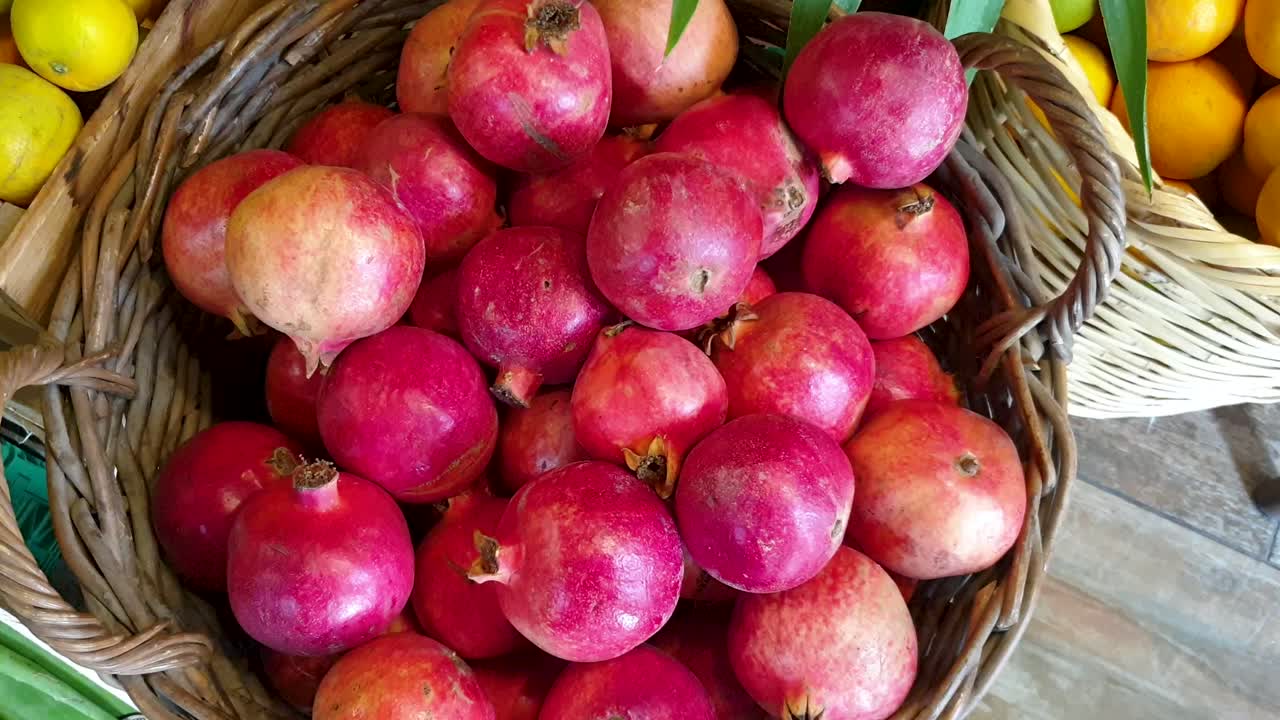 Ovenfra-udsigt af fletkurv fyldt med farverige, friskplukkede, modne lokalt dyrkede granatæbler i en frugt- og grønthandel