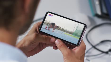 compuesto de un médico masculino viendo un evento de atletismo en un teléfono inteligente