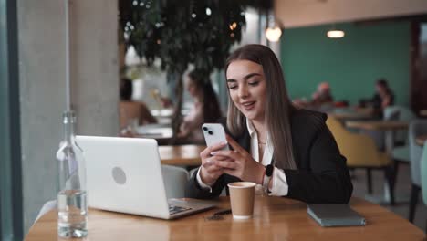 Hermosa-Mujer-Sentada-En-Un-Café-Vestida-De-Negocios-Con-Una-Computadora-Portátil,-Enviando-Mensajes-Alegremente-En-Las-Redes-Sociales-Y-Mensajeros-Con-Una-Sonrisa-En-Su-Rostro.