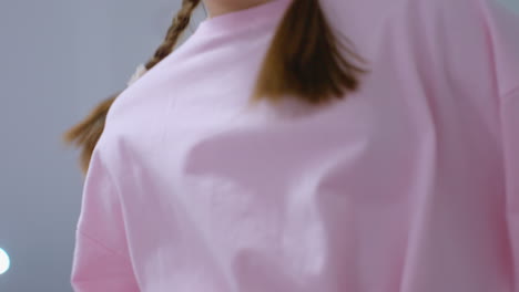 close-up of young girl in pink mid-jump during workout session, hair lifted by motion, with blurred background featuring gym interior and bright ceiling lights reflecting on glass panels