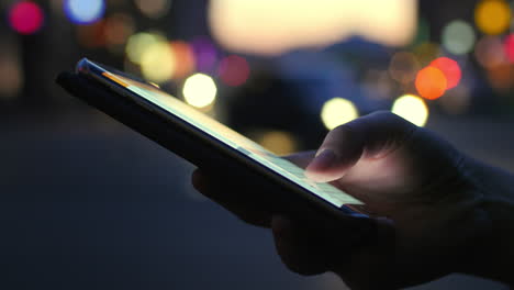 Close-up-view-of-lighting-smartphone-against-evening-road-with-cars-light-background