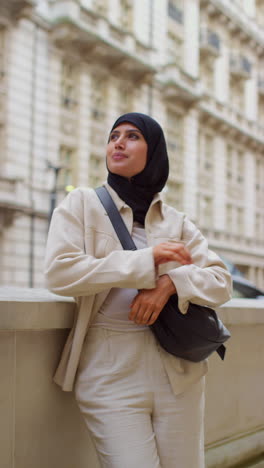 Vertical-Video-Portrait-Of-Smiling-Muslim-Businesswoman-Wearing-Hijab-And-Modern-Business-Suit-Standing-And-Folding-Arms-Outside-City-Office-Buildings