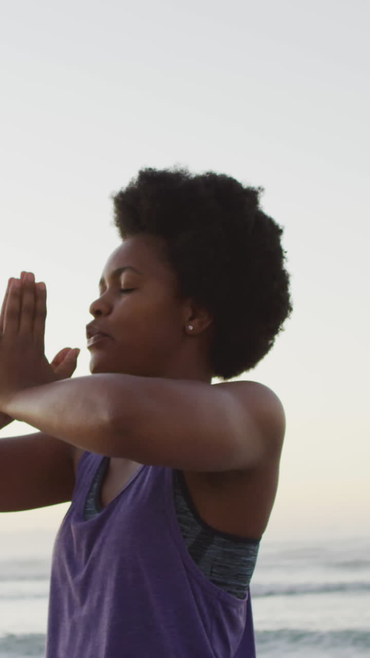 African american woman practicing yoga and meditating on sunny beach