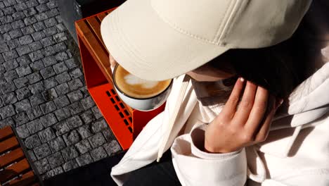 girl hold cup of latte with foam art and take sip while sit on outdoor bench