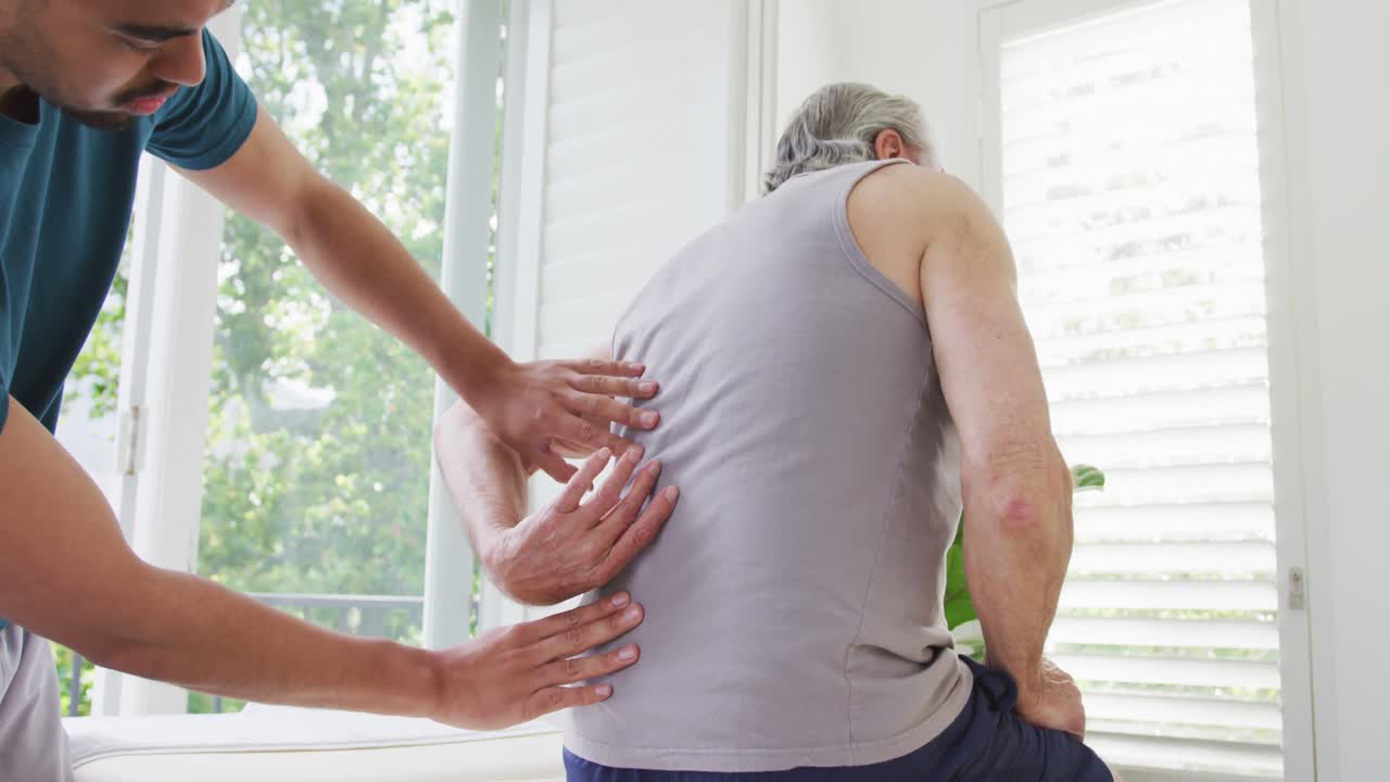Slow motion shot of male caregiver examining retired senior man's spine at nursing home