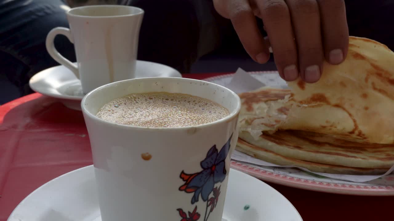 A close-up view of a delicious breakfast showcasing paratha and tea at a vibrant local street restaurant.