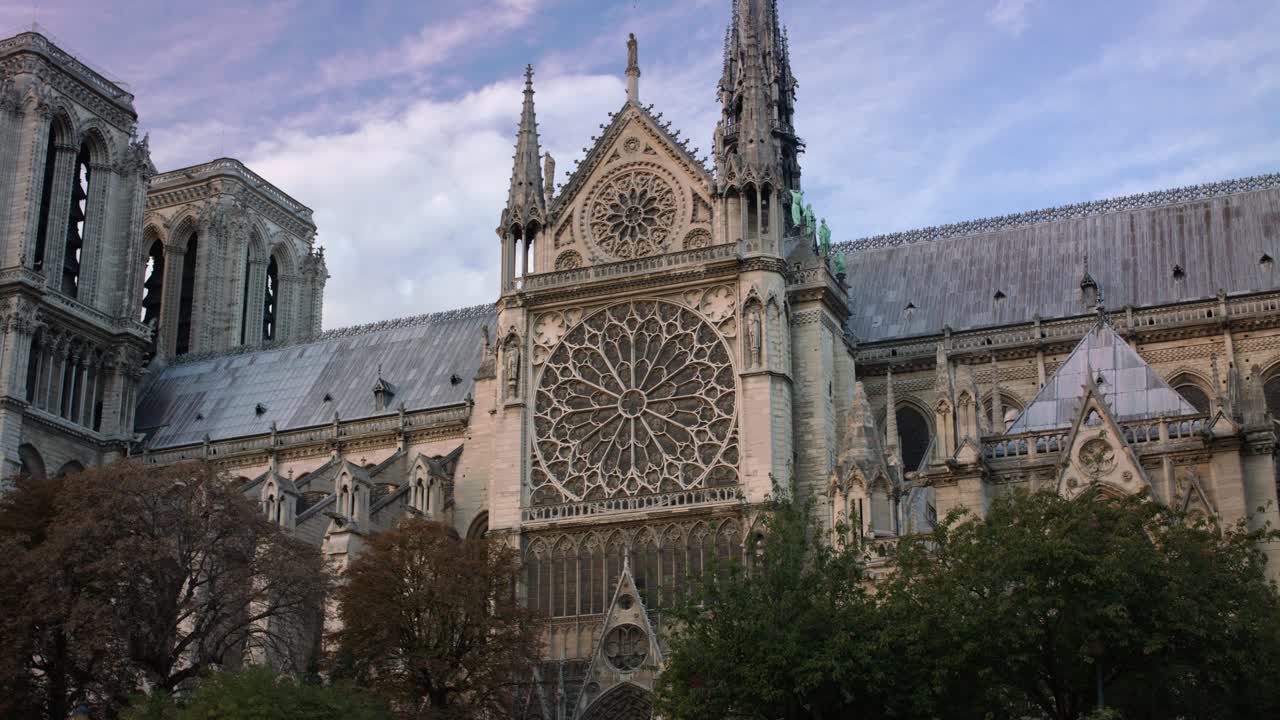 Notre-Dame Cathedral in Paris showing its stunning Gothic architecture, including the detailed rose window and twin towers. The historic building is surrounded by trees and sky