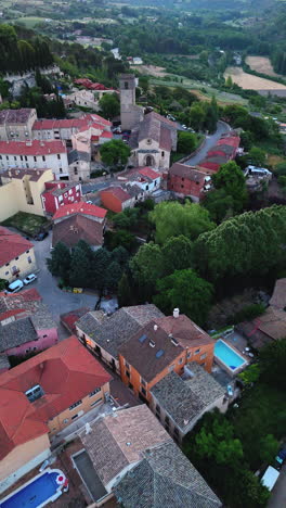vertical reverse drone clip over brihuega, la alcarria, spain. the flight reveals tiled rooftops, village houses, swimming pools, trees, a romanesque church and rural landscape in morning light