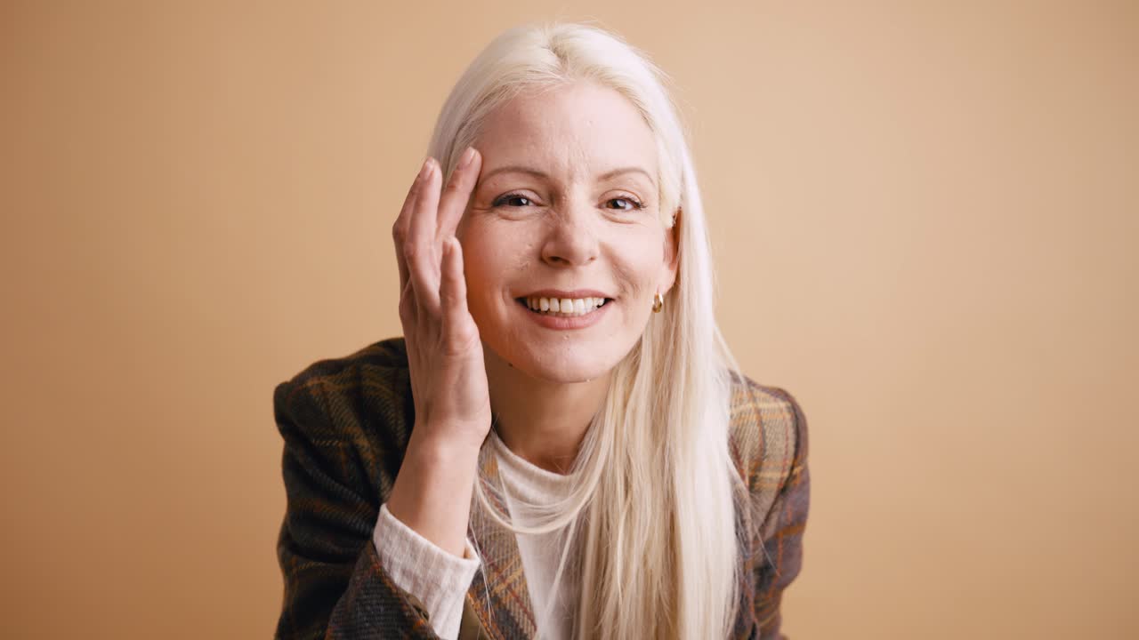 Happy Blonde Woman Smiling and Touching Her Hair in Studio