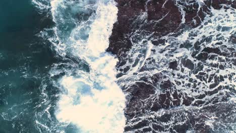 the agressive waves splashing against the rocky shore with a fisherman on the rock