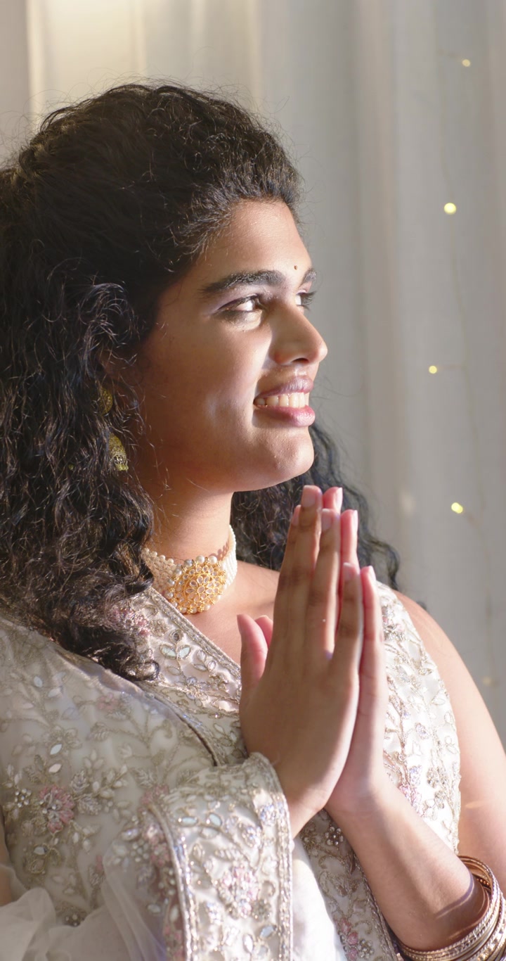 Vertical video: Adult Indian woman starting folded hands, praying in soft lit room in saree