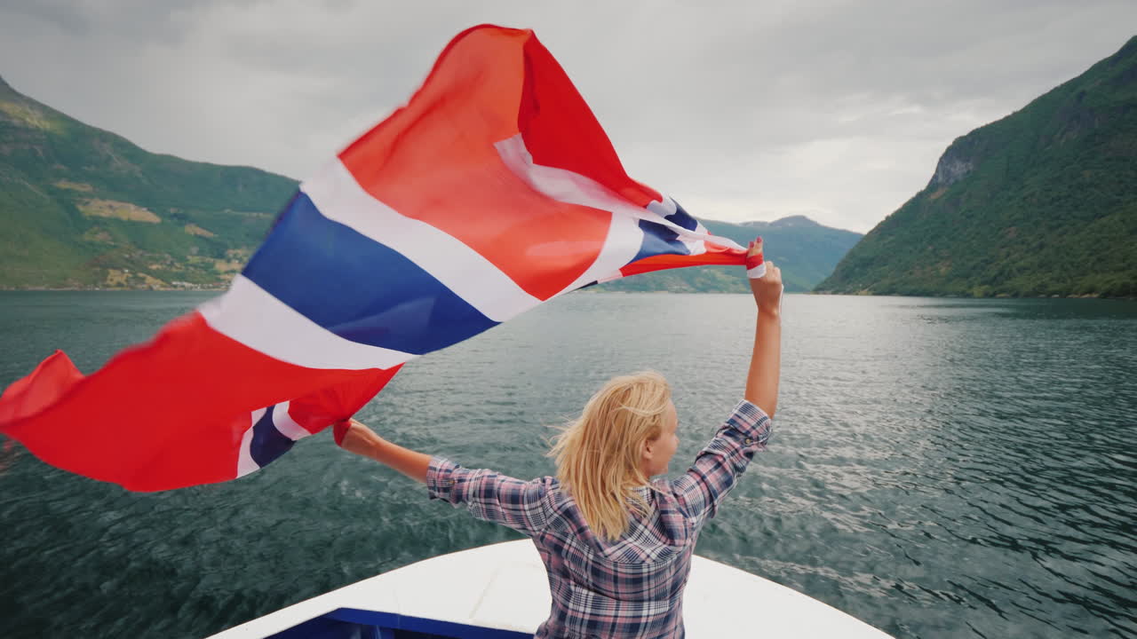 큰 노르웨이 국기를 든 활동적인 여성이 2018년 유람선 피요르드 유람선의 뱃머리에 서 있습니다.