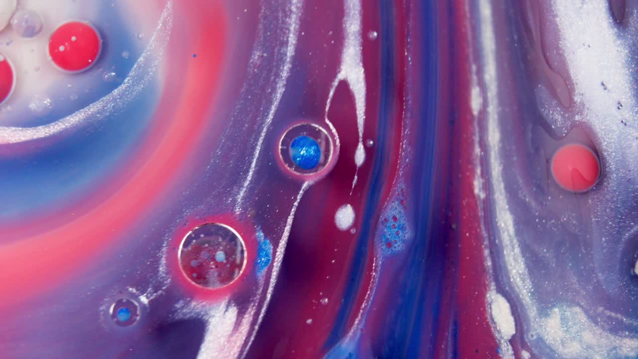 Tinta líquida arremolinándose y fluyendo con colores azul, rojo, morado y blanco.