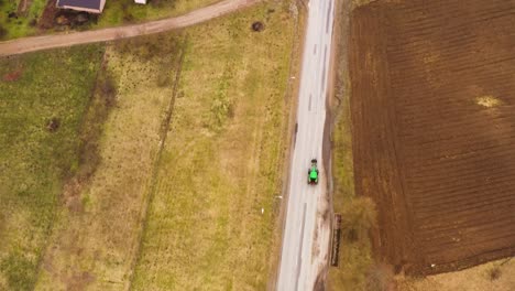 green tractor driving on a countryside road passing houses, drone view