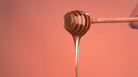 super slow motion cu honey pouring from honey stick against bright background