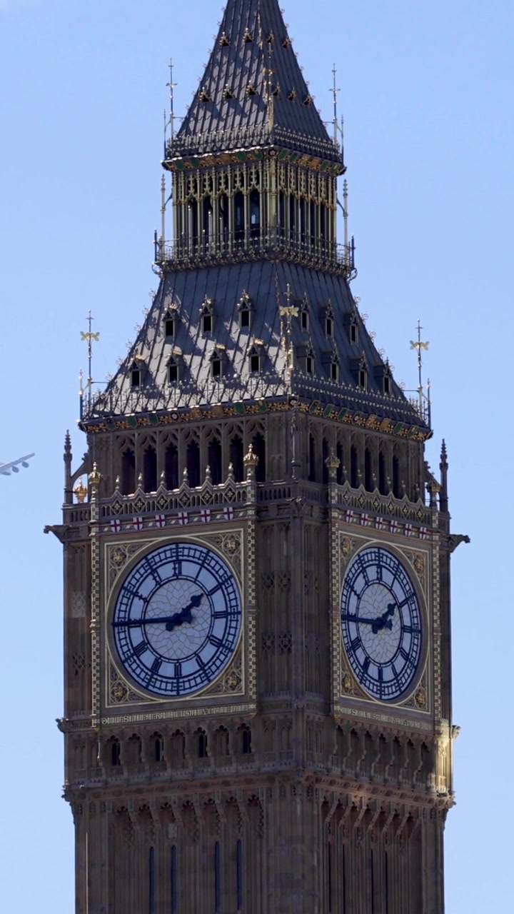 A vertical shot focusing on the historic clock tower as an airplane flies past.