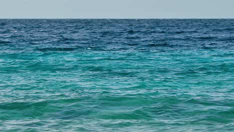 las fuertes ondas de la corriente oceánica ruedan hacia la orilla mostrando un gradiente de agua verde a azul profundo oscuro.