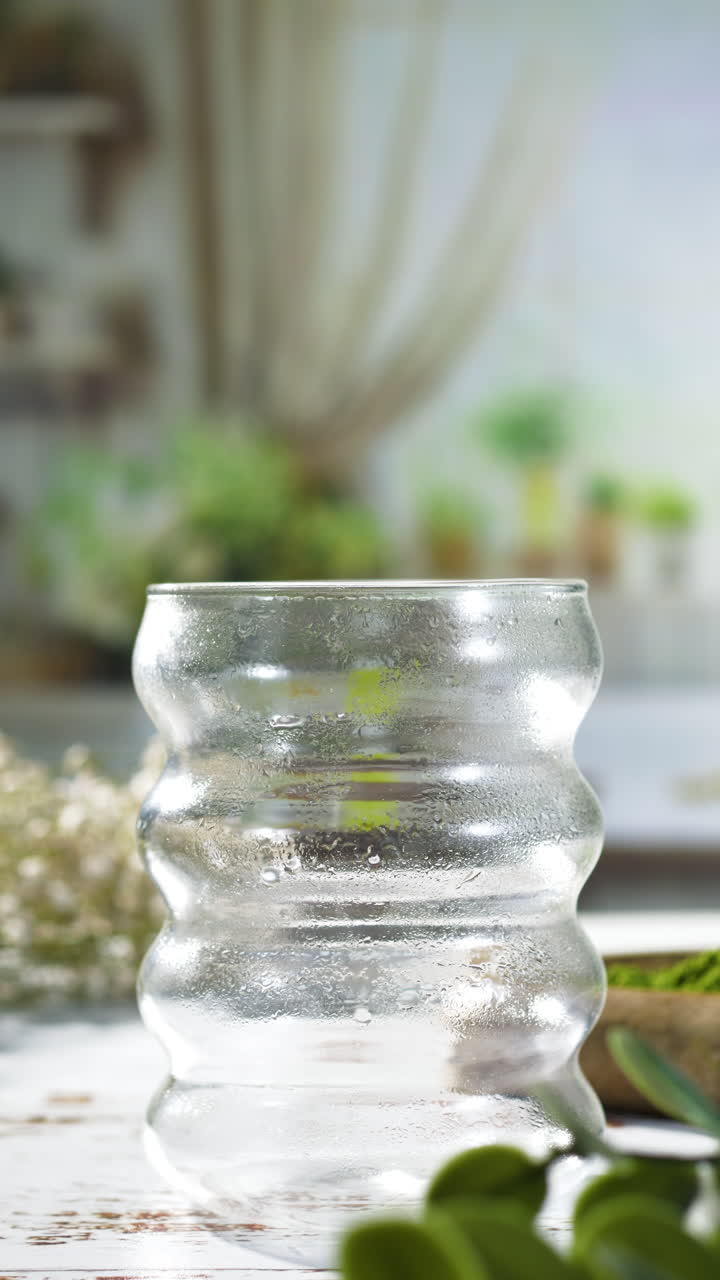 A creative stopmotion shows strawberry jam, ice cubes, milk, and matcha tea sequentially layered into a textured glass, forming a colorful iced matcha strawberry latte in a cozy kitchen setting.