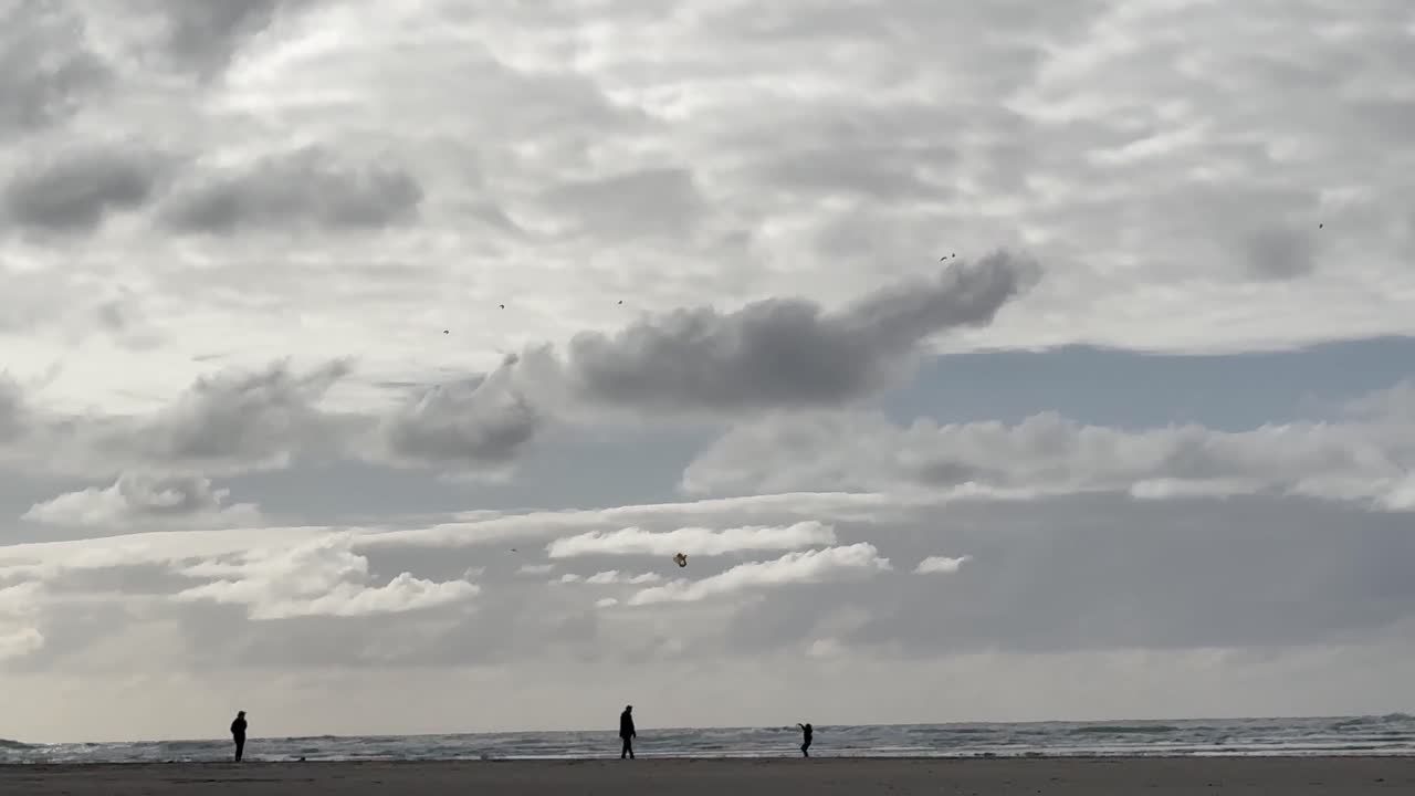 오리건 해안 위의 구름이 가득한 하늘과 가족의 실루이 해변에서 유니폼을 입고 재미있게 날아다니고 있습니다.