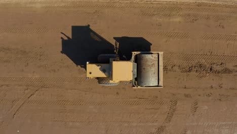 top down following aerial shot of a bulldozer roller compacting dirt on a sunny day