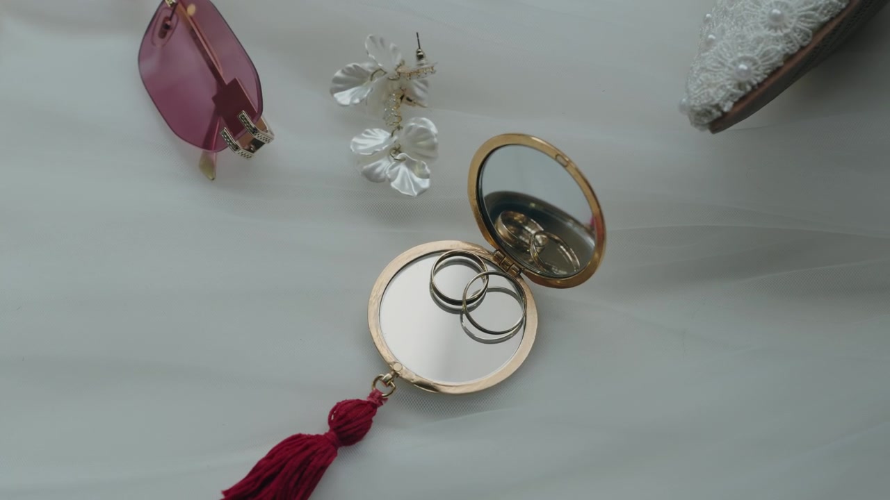 Dua Cincin Kawin Emas Dalam Cermin Kompak Bulat Di Samping Anting Dan Kacamata Hitam Tata Letak Datar