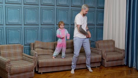 Happy-funny-family-father-and-child-kid-daughter-dancing,-jumping-on-sofa,-listening-music-at-home