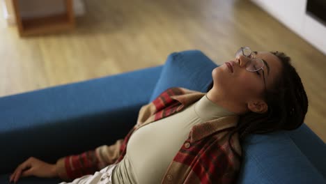 exhausted african american woman in eyeglasses lay down on sofa