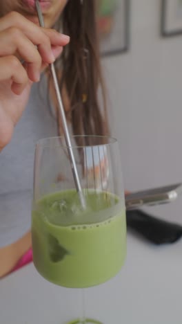 person stirring an iced matcha latte in a wine glass