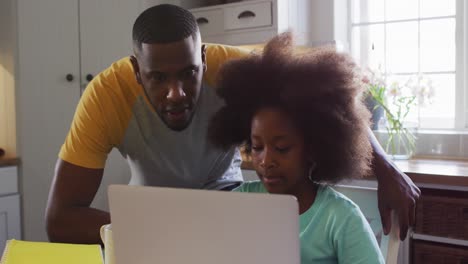 Hija-Afroamericana-Y-Su-Padre-Usando-Una-Computadora-Portátil-Juntos-En-La-Mesa-De-La-Cocina