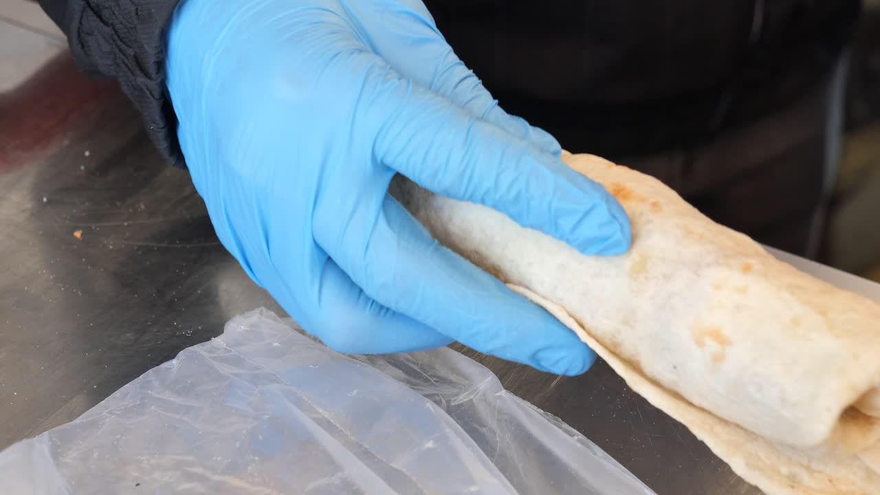 una persona con guantes azules está preparando un envoltorio de shawarma