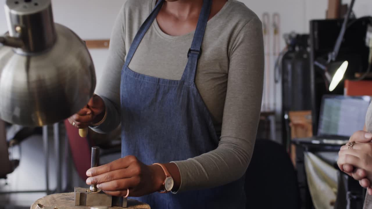 African american female worker shaping jewellery with hammer in studio in slow motion