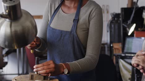 African-american-female-worker-shaping-jewellery-with-hammer-in-studio-in-slow-motion