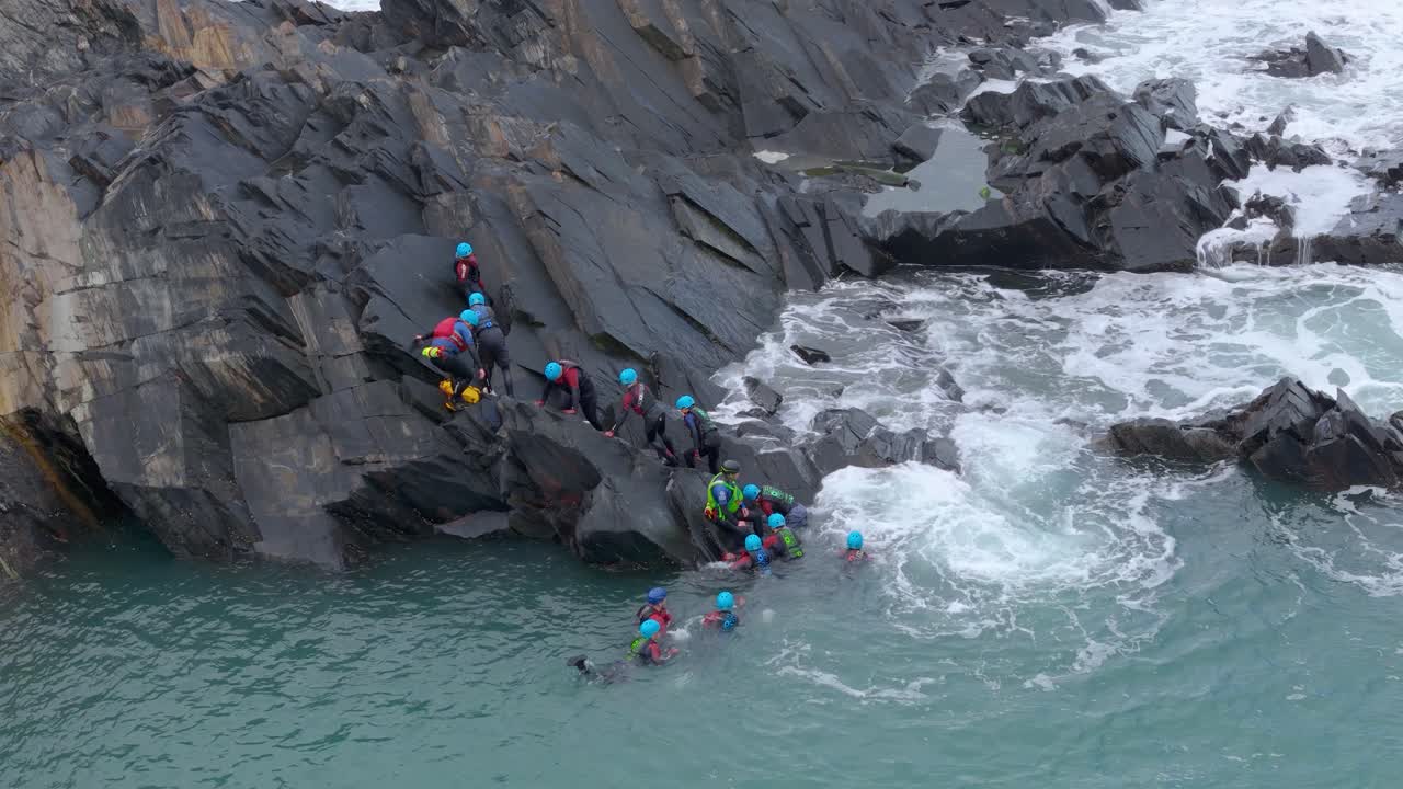 Coasteering Adventure: Group of People Climbing Rocks and Jumping into the Ocean