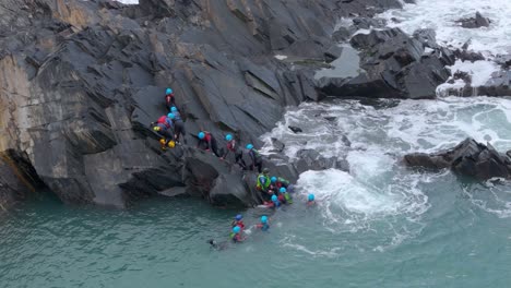 coasteering adventure: group of people climbing rocks and jumping into the ocean