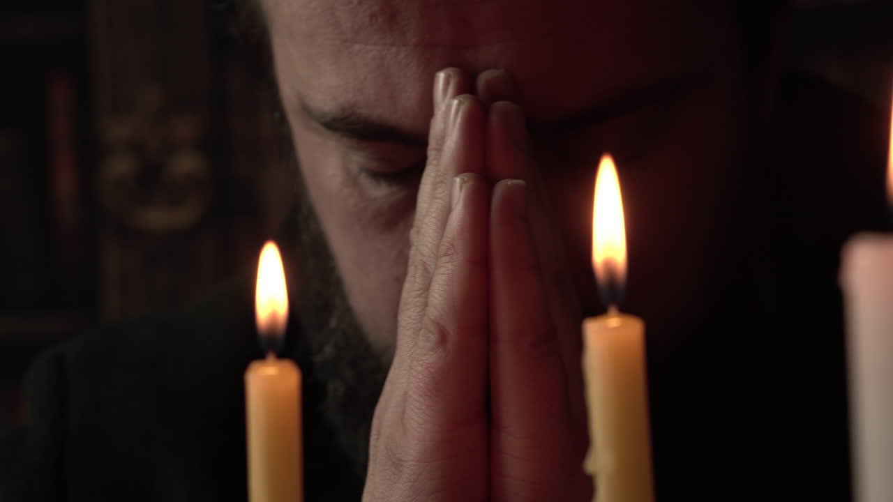 Homem religioso orando a Deus em frente a velas com as mãos postas, close-up.