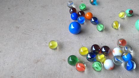 lots of bright rolling marbles collide on a concrete floor in slow motion