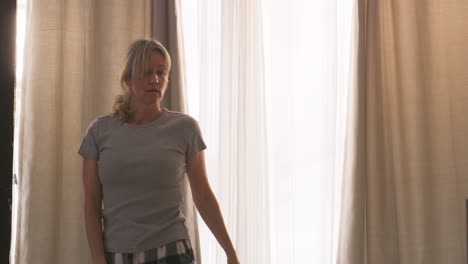 woman opening curtains in bedroom