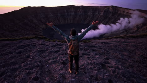 hiker with outstretched arms overlooking a smoking volcanic crater at sunrise