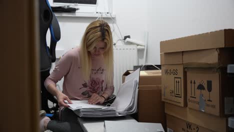 a young lady checks documents in a room full of cardboard boxes ready for the move