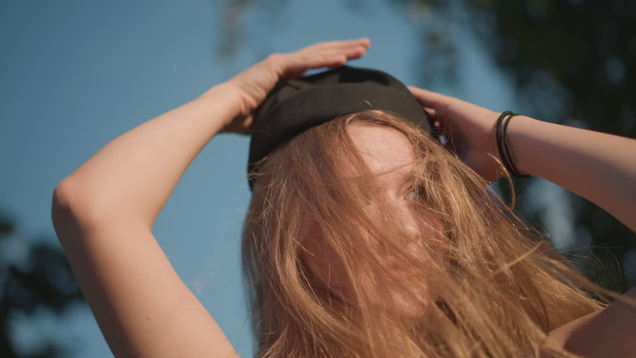 prato soleggiato, donna caucasica che gioca con i capelli, ritratto ravvicinato, modella che inclina la testa, si toglie il cappello, luce dorata, brezza al rallentatore, sorriso spontaneo, atmosfera intima, movimento delicato, tonalità della pelle calde, delicato