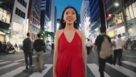 a woman wearing a vibrant red dress confidently crosses a bustling urban intersection during twilight. the lively environment features numerous pedestrians and bright city lights.